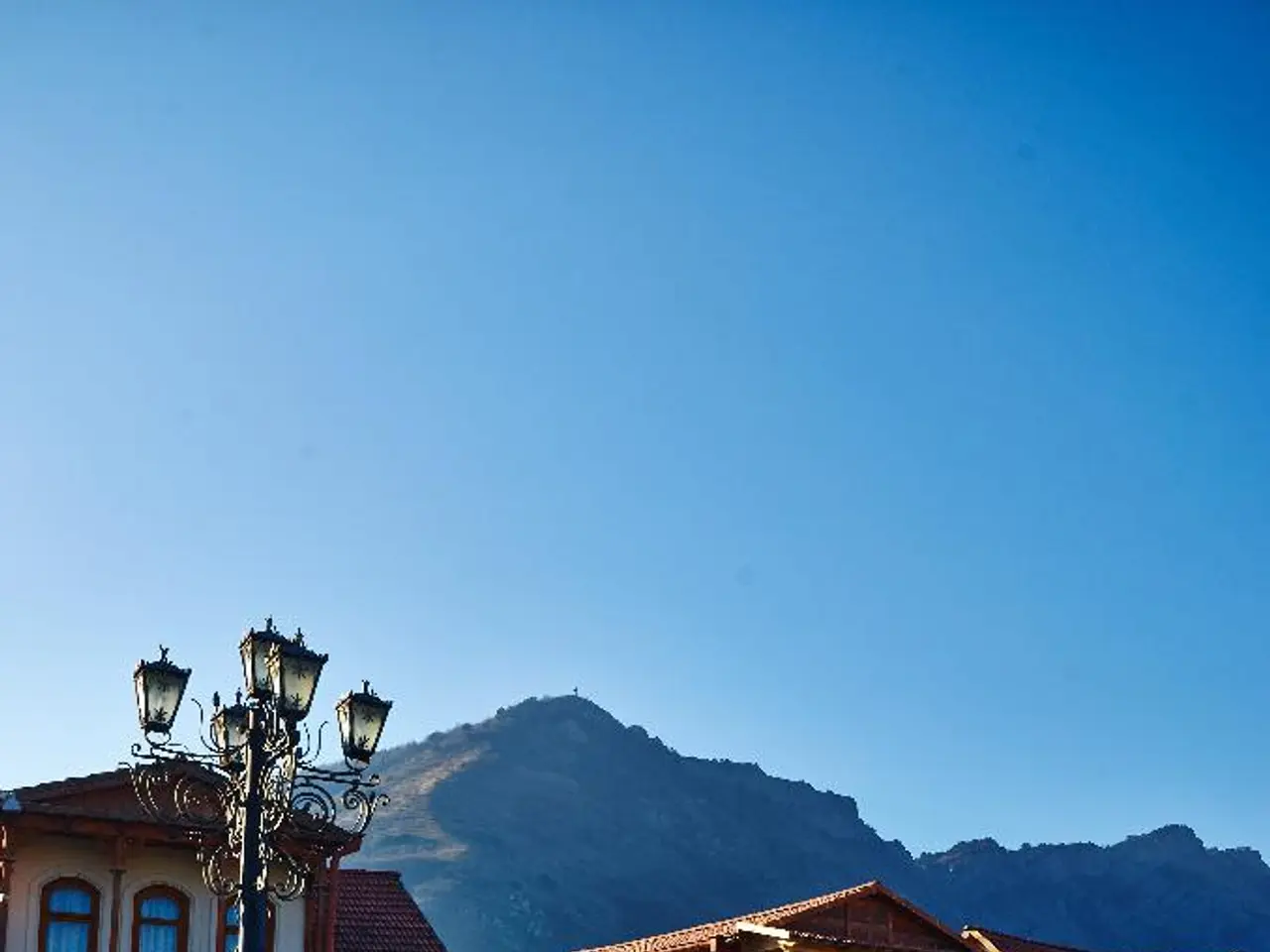 This picture shows few houses and we see pole lights and a hill and we see a blue sky.