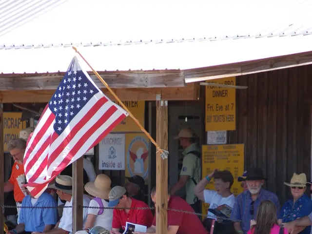 There is a flag attached with the pole. In the background, there are group of people. Some of them...