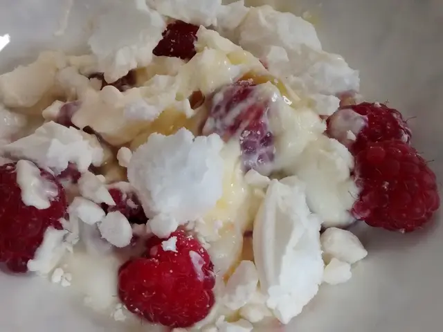 In this image there is a food item in the bowl. There are a few raspberries and there is cream.