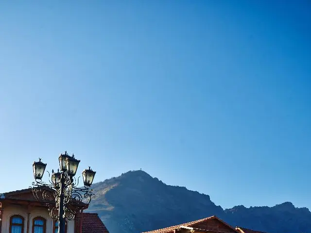 This picture shows few houses and we see pole lights and a hill and we see a blue sky.
