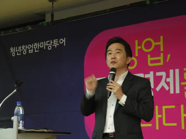 In this picture one is standing and wearing a black suit and white shirt and microphone in his...